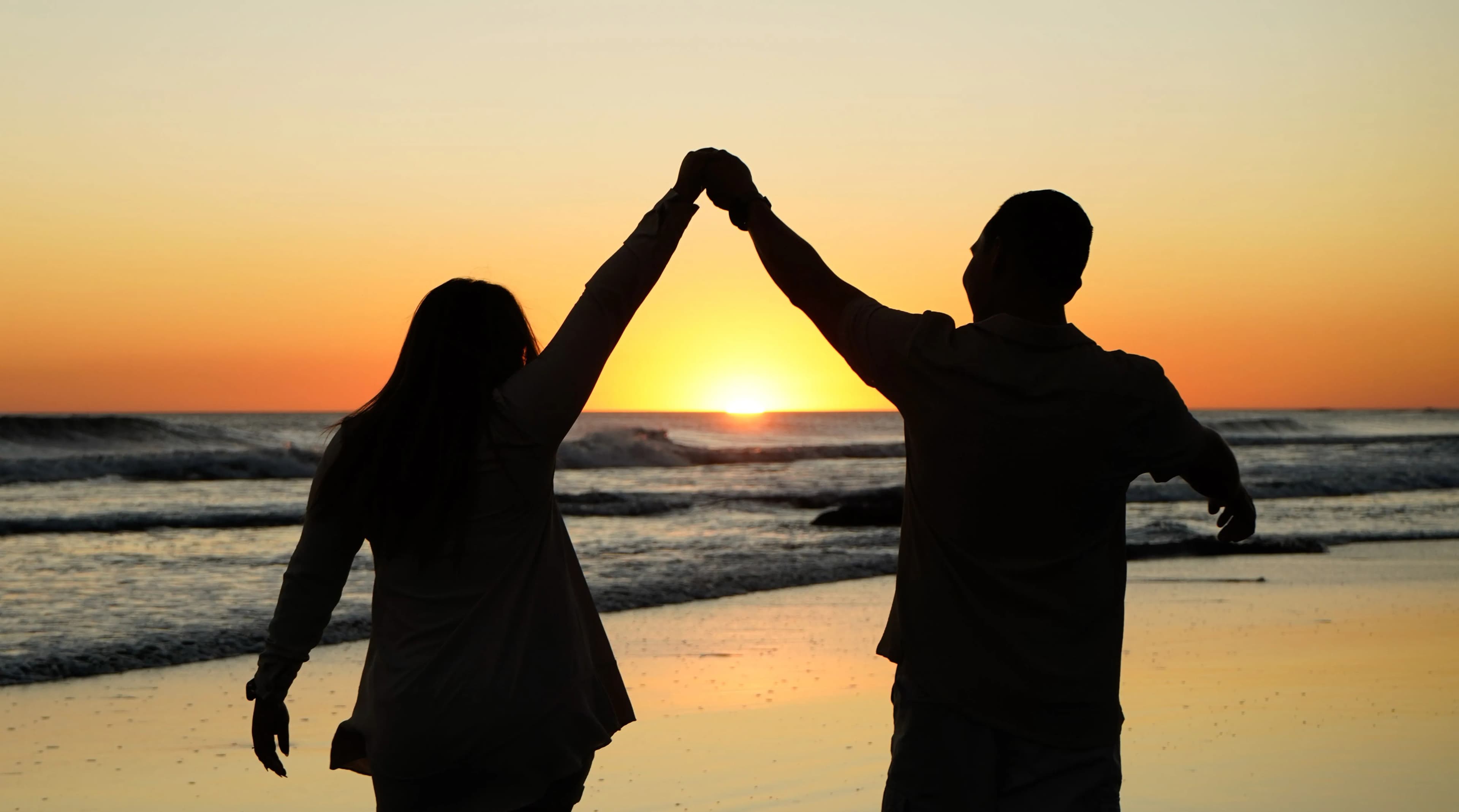 A person standing with arms raised against a warm sunset sky